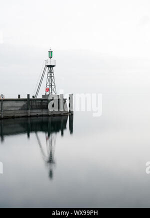 Clignotant et mur du port sur les eaux du lac calme sous un ciel couvert l'espace négatif abstract Banque D'Images