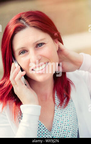 Portrait of smiling belle jeune femme assise sur un banc avec un téléphone mobile, contre l'arrière-plan de l'été parc verdoyant. Banque D'Images