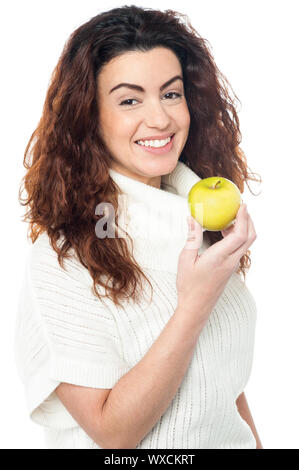 Femme debout sur le côté joyeux qui posent avec une pomme dans la main, regardant la caméra. Banque D'Images