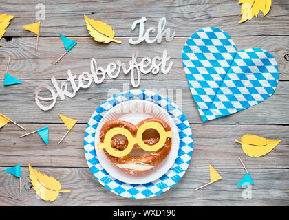 Texte papier 'J'aime' Oktoberfest en allemand, mise à plat sur une table en bois rustique avec les bretzels sur la plaque de papier décoratif, coeurs, drapeaux et les feuilles d'automne. Banque D'Images