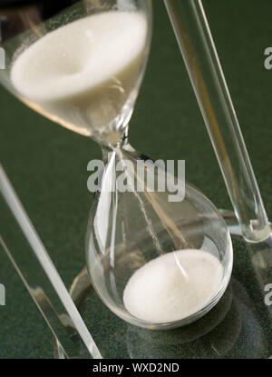 Sable tombe vers le bas à travers un cristal de verre heures assis sur le dessus de table Banque D'Images