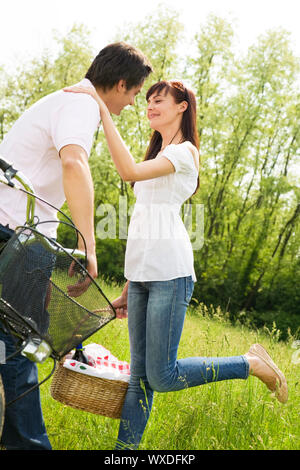 Couple in park with holding panier à pique-nique, des baisers. Femme soulève sa jambe Banque D'Images