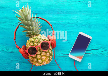 Drôle d'ananas, des lunettes de soleil et d'écouteurs peint en bleu. Mise à plat sur papier rouge fond avec boules moelleuses et rétro des bandes audio. Banque D'Images