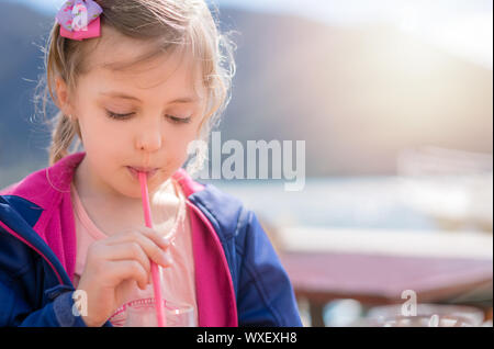 Cute little girl de boire du jus de fruits à l'aide de la paille Banque D'Images