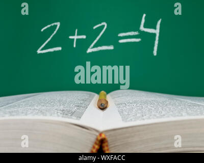 2  + 2  = 4 écrit sur une ardoise avec un livre ouvert et un crayon sur le premier plan. Banque D'Images