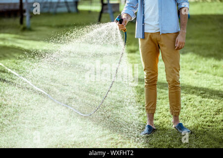 Man watering pelouse verte, en répandant de l'eau sur l'herbe avec pistolet à eau, close-up avec pas de visage Banque D'Images