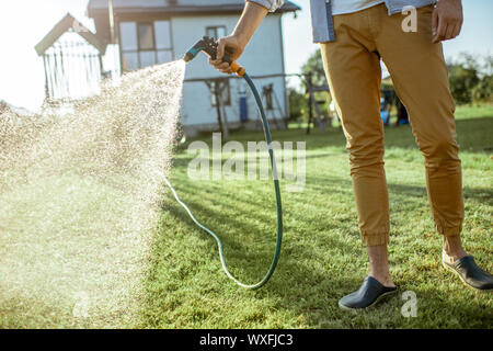 Man watering pelouse verte, en répandant de l'eau sur l'herbe avec pistolet à eau, close-up avec pas de visage Banque D'Images