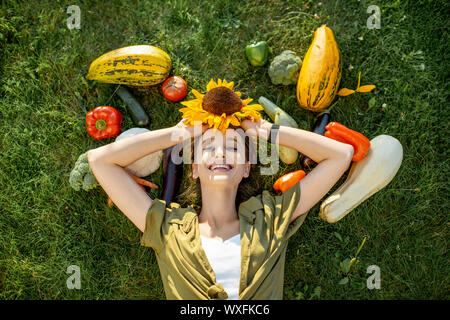 Young smiling woman couché dans l'herbe entouré par des légumes fraîchement ramassés. Concept d'aliments sains Banque D'Images