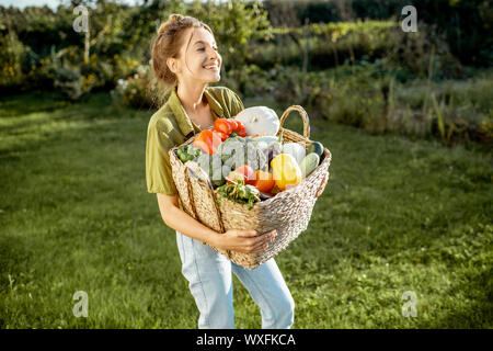 Portrait d'une belle jeune femme avec panier plein de légumes fraîchement cueillis dans le jardin permanent sur une soirée ensoleillée Banque D'Images