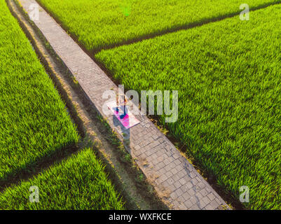 Jeune femme pratiquer le yoga en plein air les champs de riz le matin au cours de retraite bien-être à Bali. Vue depuis le bourdon Banque D'Images