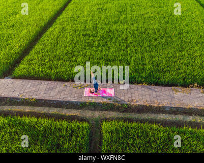 Jeune femme pratiquer le yoga en plein air les champs de riz le matin au cours de retraite bien-être à Bali. Vue depuis le bourdon Banque D'Images