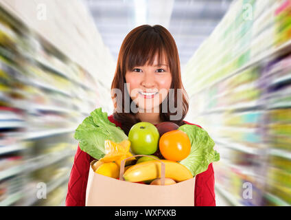 L'Épicerie asiatique. Smiling young woman holding paper panier plein de provisions dans une épicerie/supermarché . Banque D'Images