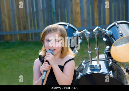 Kid blonde girl singing in tha cour avec batterie derrière Banque D'Images