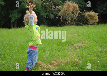 Blondie fille jouant avec l'herbe sur le champ vert. Banque D'Images