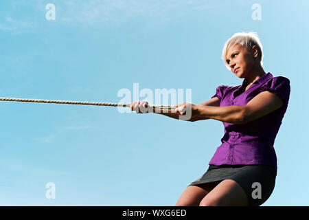 Resolute business woman pulling rope contre ciel bleu, symbole de puissance et de détermination. L'espace de copie, side view Banque D'Images