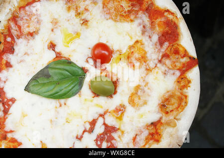 Détail d'une délicieuse pizza avec une feuilles de basilic, un olivier et une tomate fraîche comme décoration Banque D'Images