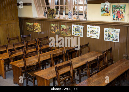 UK, County Durham, Beamish Museum, fosse, Village, École classe junior vers 1913, d'un bureau et de chaises ci-dessous ediucational matériel sur mur Banque D'Images