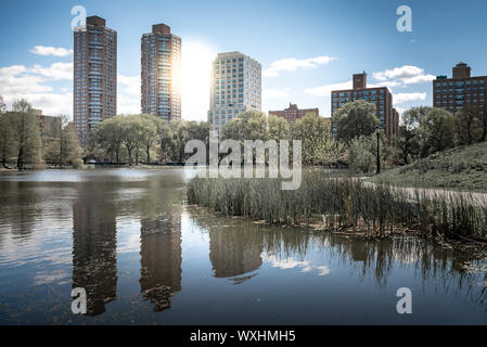 Une photo de Central Park lors d'une belle journée ensoleillée, avec ses bâtiments reflétant dans l'eau d'un lac. La ville de New York, United States Banque D'Images