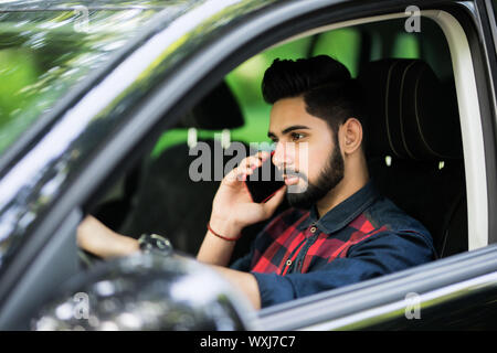 Portrait de jeune beau brun au volant voiture et parlant au téléphone mobile. Banque D'Images