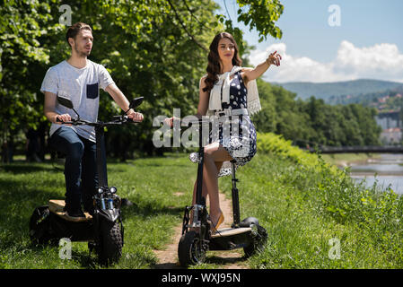 Couple sur les scooters électriques en faisant une pause par une rivière, la Bosnie-et-Herzégovine Banque D'Images