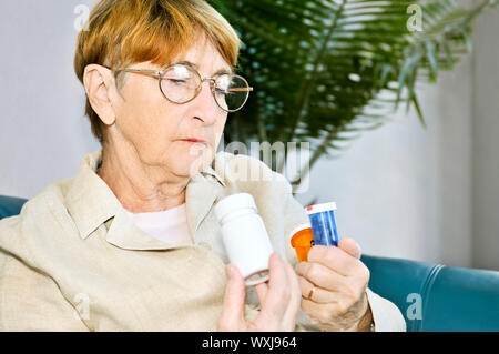 Femme âgée la lecture des étiquettes d'avertissement sur les bouteilles de pilules à l'aide de médicaments Banque D'Images