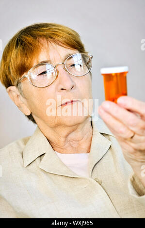 Femme âgée la lecture des étiquettes d'avertissement sur les bouteilles de pilules à l'aide de médicaments Banque D'Images