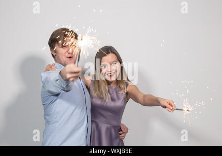 Parti, nouvelle année, noël fun et jours fériés concept - jeune couple heureux avec cierges sur fond blanc Banque D'Images