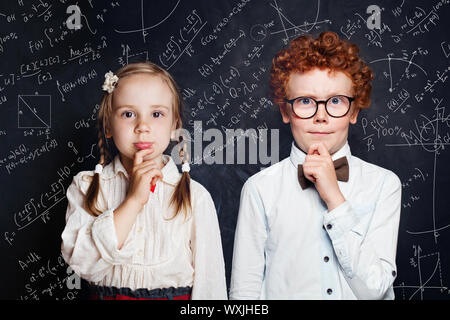 Une petite pensée aux enfants. Petit garçon et fille étudiant sur tableau noir de fond avec des formules mathématiques et sciences Banque D'Images