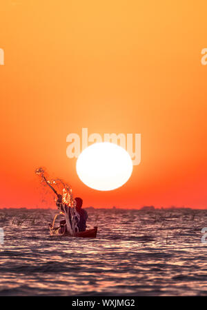 Un homme dans un kayak aviron contre le soleil sur un ciel orange au lever du soleil. De l'homme paysage rétroéclairé éclaboussures avec sa pagaie Banque D'Images