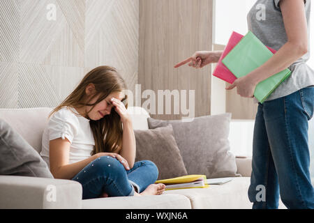 Mère fille pleurer école gronde pour faire leurs devoirs. Fille assise en tailleur sur un canapé. Banque D'Images