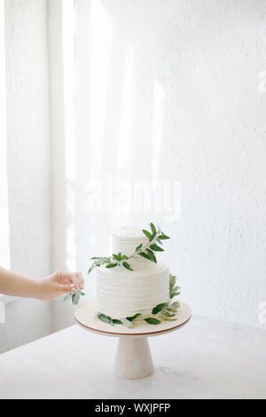 Femme décoration d'un gâteau de mariage à deux niveaux avec des branches d'olivier Banque D'Images