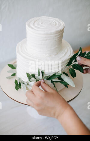 Femme décoration d'un gâteau de mariage à deux niveaux avec des branches d'olivier Banque D'Images