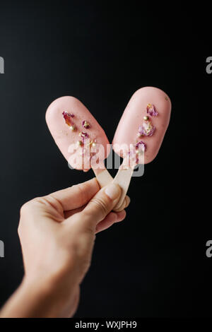 Woman's hand holding deux ice-cream Cake pops décoré avec des pétales de rose et sprinkles Banque D'Images