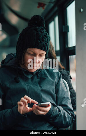 Belle femme adultes sms sur téléphone mobile en bus public en après-midi d'hiver froid Banque D'Images