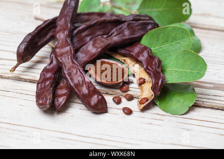 Avec la poudre de caroube. Gousses de caroube biologique avec des graines et les feuilles sur la table en bois blanc. La saine alimentation, de l'alimentation arrière-plan. Banque D'Images