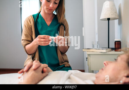 Médecin de prendre la température pour senior woman Banque D'Images