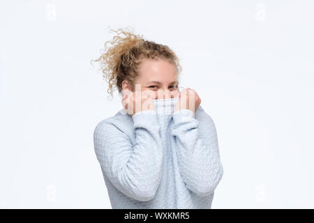 Young caucasian woman bouclés se cachant sous pull bleu être gêné. Studio shot. Banque D'Images