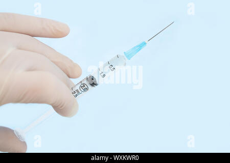 Gloved hand holding syringe sur fond bleu Banque D'Images