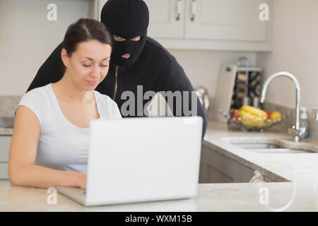 Woman using laptop while burgler est à regarder dans la cuisine Banque D'Images