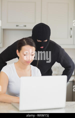 Burglar looking at le portable derrière woman in kitchen Banque D'Images