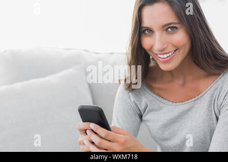 Portrait d'une femme textos alors qu'elle est assise sur un canapé Banque D'Images