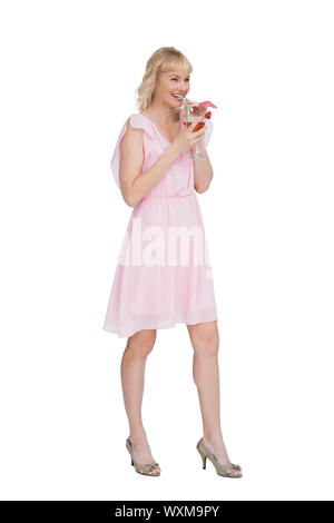 Cheerful blonde posing while drinking cocktail against white background Banque D'Images