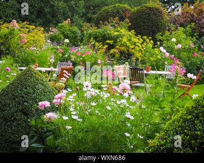 Belles fleurs d'été dans un jardin de campagne anglaise à Chenies Manor, Bucks. .Rose, Blanc et vert pâle autour de tables et de chaises en bois. Banque D'Images