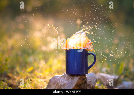 Bleu mug de thé ou café au lait, à l'extérieur, le concept du voyage, gerbe, splash. Les reflets sur les photos du coucher de soleil, bokeh agréable Banque D'Images