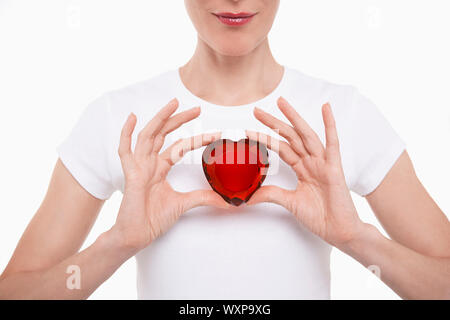 Portrait Gros plan d'une femme en blanc tshirt holding red glass heart against white background Banque D'Images