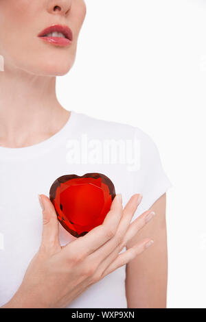 Portrait Gros plan d'une femme en blanc tshirt holding red glass heart against white background Banque D'Images