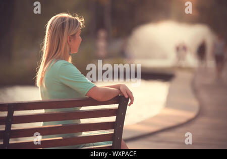 Femme aux cheveux blonds réfléchir dans le parc. Femme assise sur un banc Banque D'Images