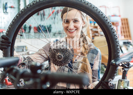 Très heureux mécanicien vélo femme regardant à travers la roue de bicyclette Banque D'Images