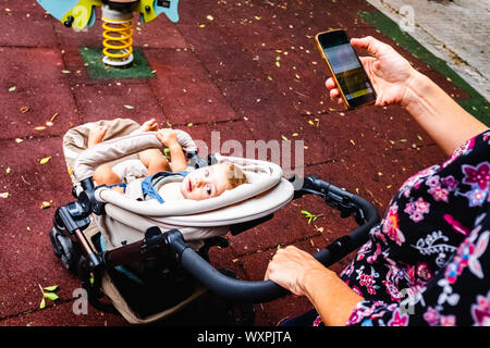 Promenades mère son bébé en présence de distractions utilise son smartphone travaillant sur le multitâche. Banque D'Images