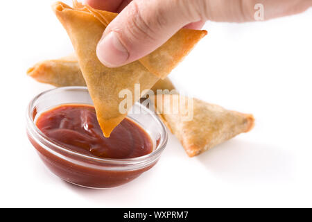 La main avec samosa trempant dans une sauce aigre-douce isolé sur fond blanc. La nourriture traditionnelle indienne Banque D'Images